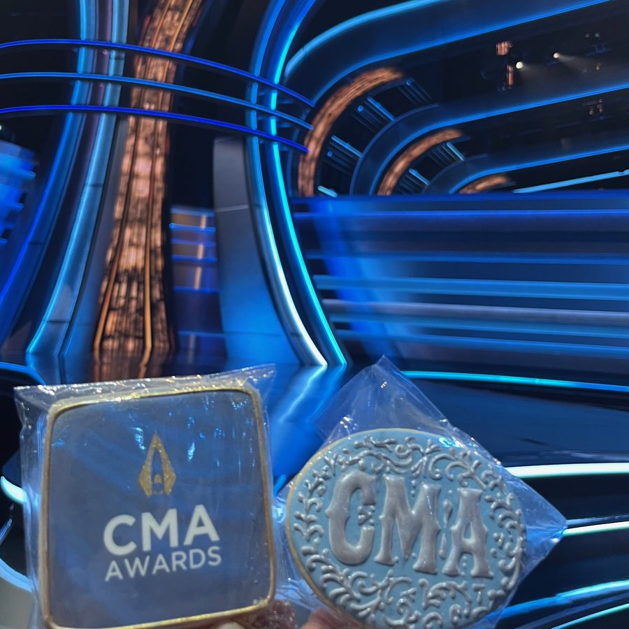 Two wrapped CMA Awards cookies held up on the awards stage: one printed with the official logo, one hand-piped with ornate silver lettering