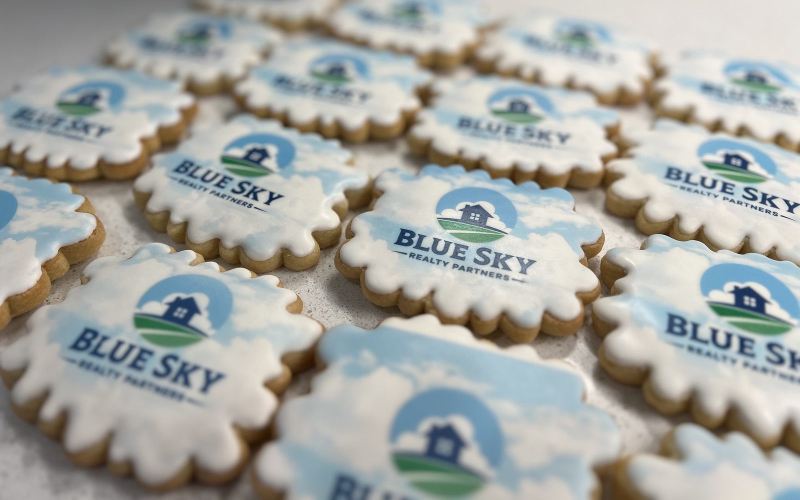 Scalloped cookies printed with the Blue Sky Realty Partners logo on a sky-blue background